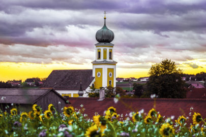 Kirche Michelsneukirchen mit lilafarbenen Himmel und gelb-leichtenden Sonnenblumen im Vordergrund.