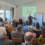 Referent erklärt und zeigt auf eine Tafel; Workshop-Besucher hören zu