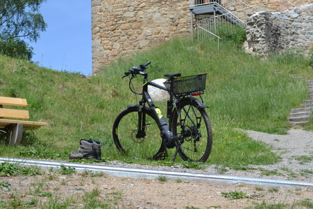 Rad und Wanderstiefel im Hintergrund Burgruine und Sitzbank